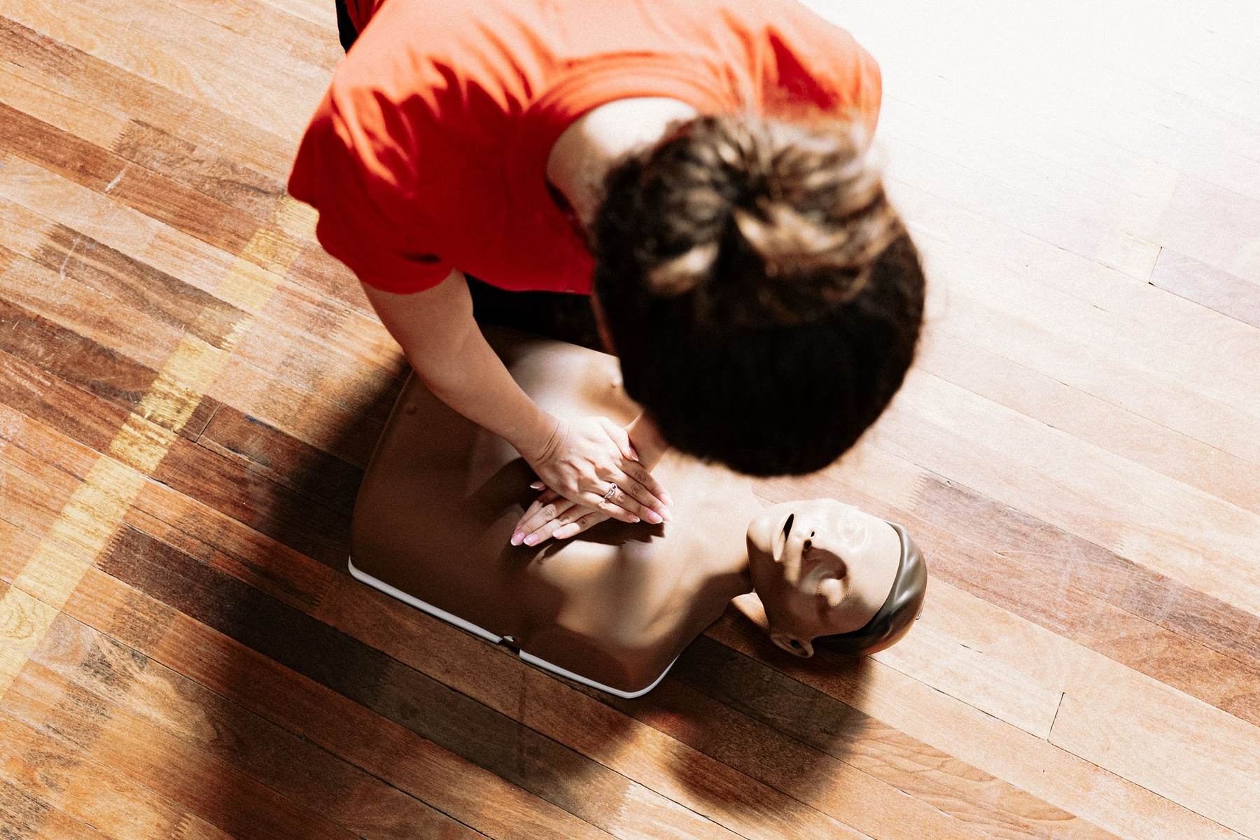 Instructor demonstrating CPR on a training manikin on a wooden floor