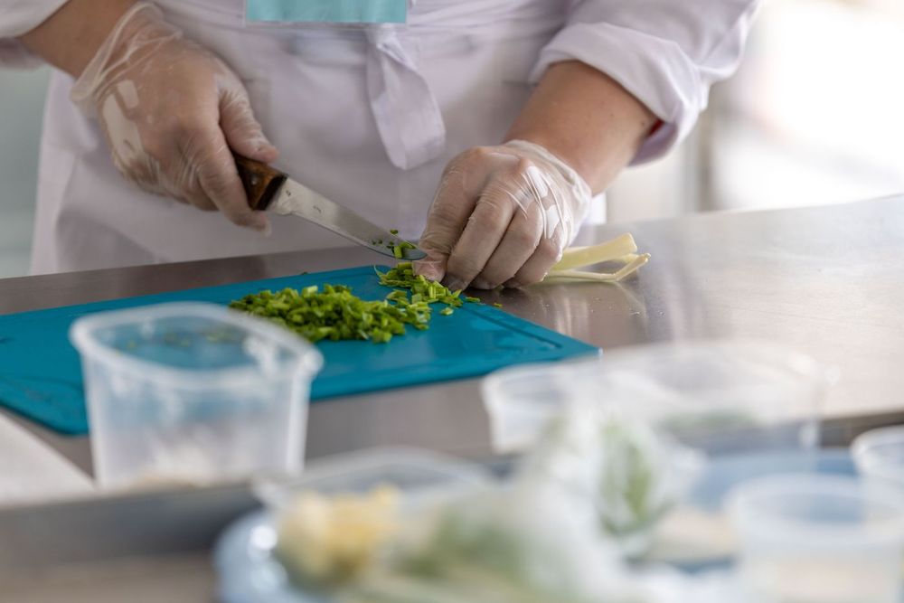 Gloved hands chopping herbs on a clean food preparation surface