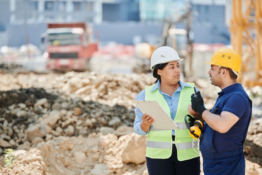 Two site workers in hard hats and high-visibility vests reviewing a plan